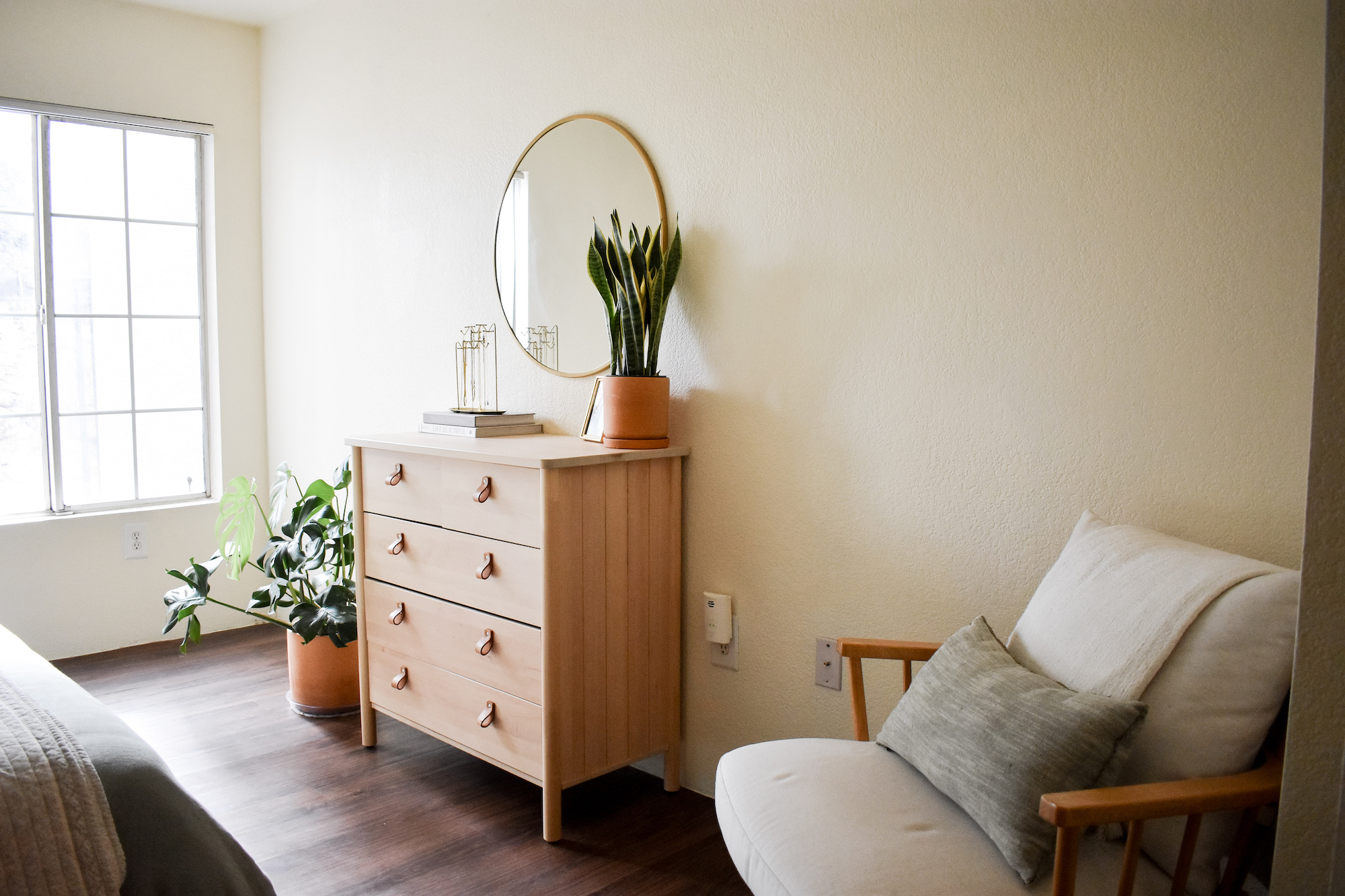 Bedroom area showing neutral dresser with mirror and plants around and light chair in corner